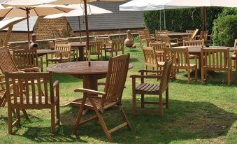 an outdoor dining area with several wooden tables and chairs , surrounded by lush greenery and umbrellas at Bartholomew Arms