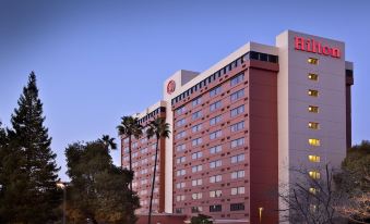 a large red and white hilton hotel with palm trees in front of it , set against a blue sky at Hilton Concord