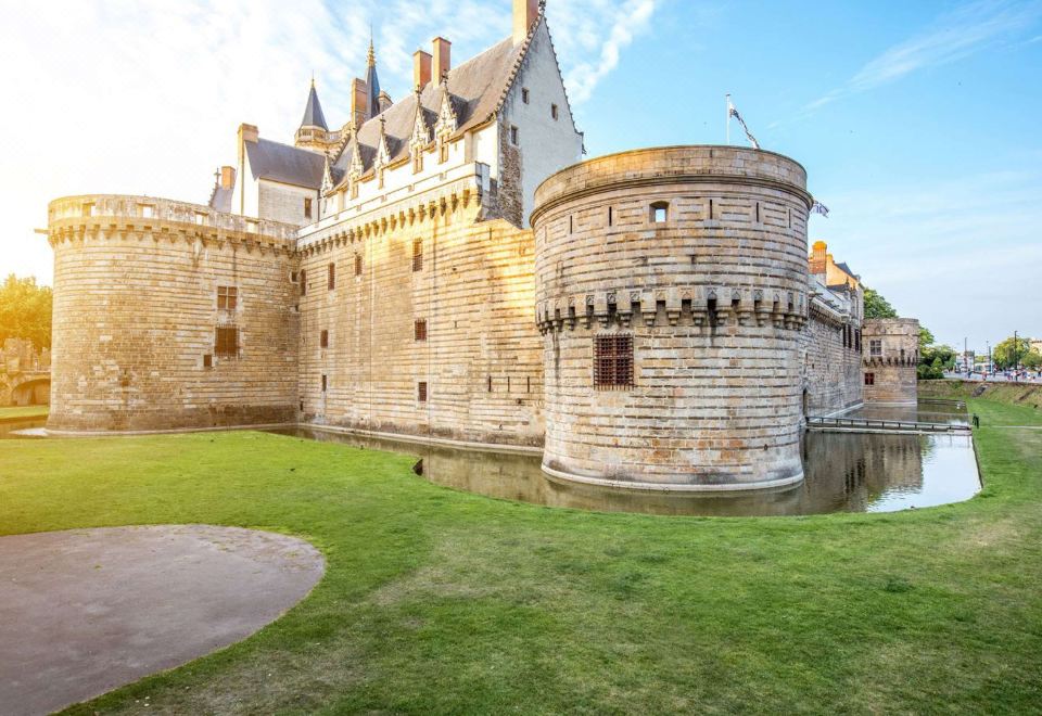 a large stone castle with a moat in front of it , surrounded by green grass at Ibis Nantes Saint-Herblain