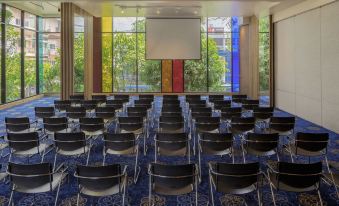 A room with blue carpet and large windows is set up with tables and chairs for an event at MeStyle Museum Hotel