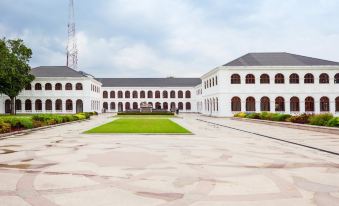 a large white building with a courtyard in front of it , surrounded by grass and trees at Capital Villa