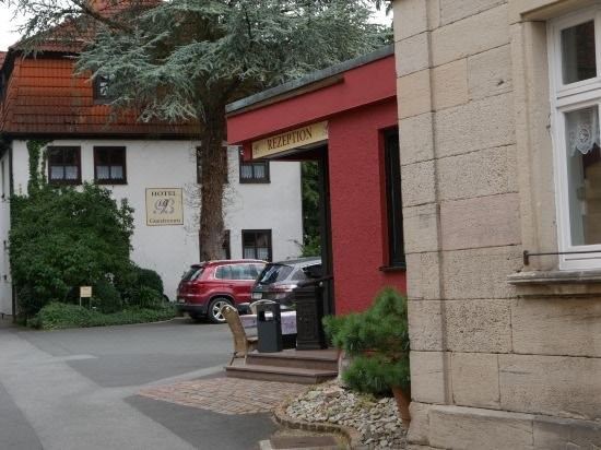 a brick building with a red door and a sign above it , next to a tree and a building with parked cars at Hotel Bauer