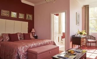 a well - decorated bedroom with pink walls , white beddings , and wooden furniture , including a coffee table and chairs at Corse Lawn House Hotel