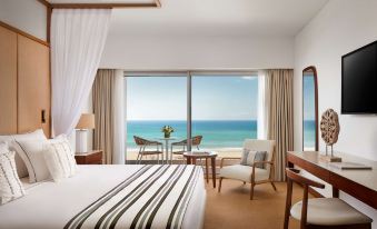 a hotel room with a bed , chair , and table in front of a large window overlooking the ocean at Tivoli Marina Vilamoura