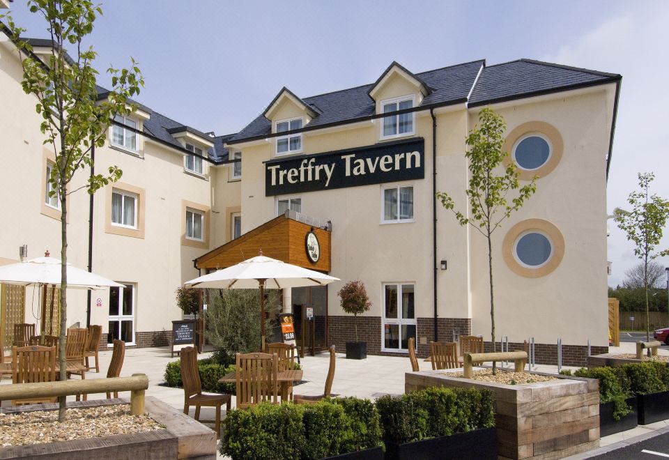 a large hotel with a wooden deck and tables set up for outdoor dining , including a white umbrella at Premier Inn Newquay (Quintrell Downs)