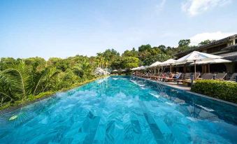 a large outdoor pool surrounded by lush greenery , with several lounge chairs and umbrellas placed around the pool area at Lahana Resort Phu Quoc & Spa