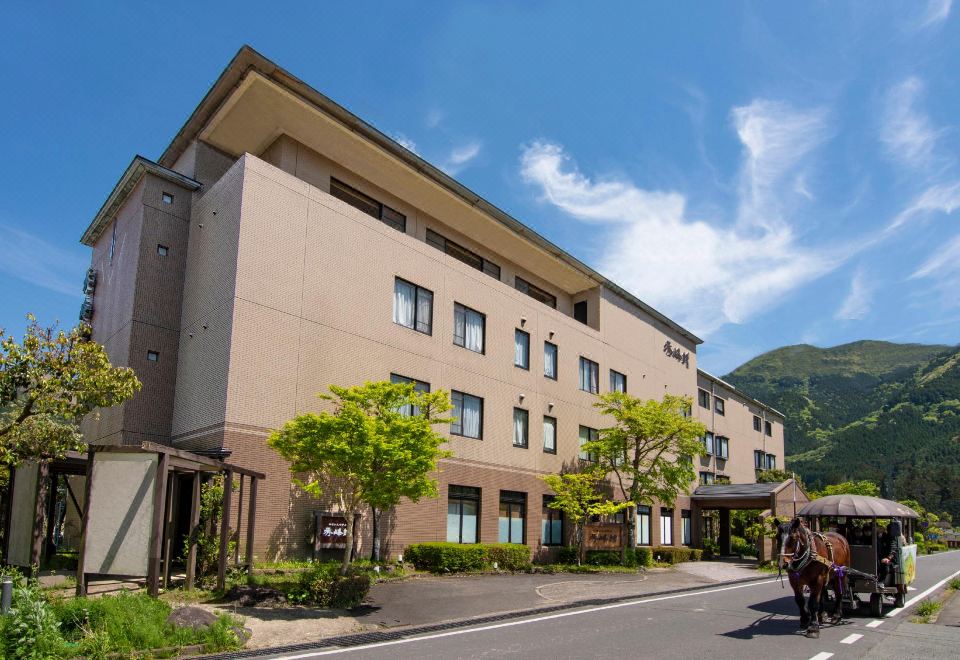 a large hotel building surrounded by trees and grass , located on a street with a car parked in front at Yufuin Hotel Shuhokan