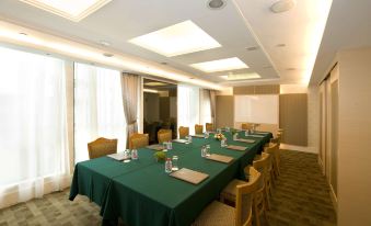 A spacious meeting room is equipped with green chairs and long tables arranged for a capacity of 10 individuals at Bishop Lei International House