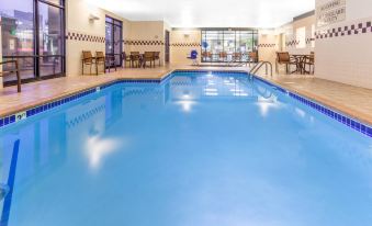 an indoor swimming pool with blue water , surrounded by chairs and tables , in a hotel room at SpringHill Suites Minneapolis Eden Prairie