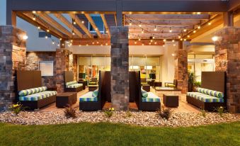 a modern , well - lit outdoor area with stone walls and wooden beams , featuring several lounge chairs and a dining table at Home2 Suites by Hilton Pittsburgh/McCandless