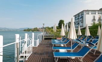 a wooden deck overlooking the water , with several blue lounge chairs and umbrellas placed around the area at Hotel Eden