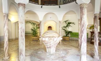 a large , white marble fountain with a palm tree in the center is surrounded by potted plants at Le Grand Hôtel