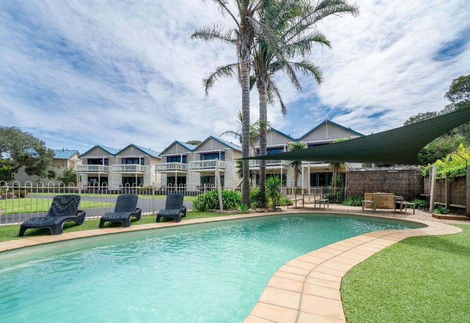 a beautiful swimming pool area with palm trees , umbrellas , and sun loungers under a clear blue sky at Boathouse Resort Studios and Suites