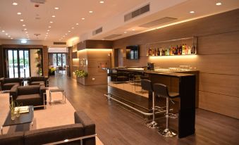 a modern bar area with a long wooden bar , several chairs , and various bottles on display at Hotel Forum