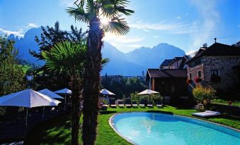 a large swimming pool surrounded by palm trees , with a mountain in the background , under a clear blue sky at Romantik Hotel Turm