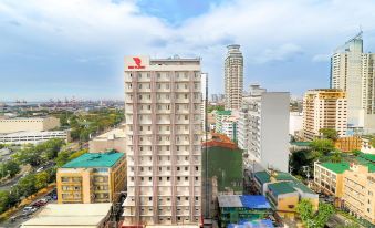 a tall building with a red logo on the side is surrounded by other buildings in a city at Red Planet Manila Bay