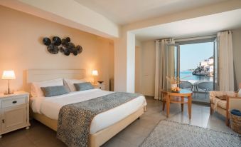 a large bed with a blue and white striped blanket is in a room with a sliding glass door leading to an ocean view at Megisti Hotel