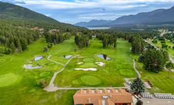 aerial view of a golf course surrounded by trees , with a lake visible in the background at Fairmont Hot Springs Resort