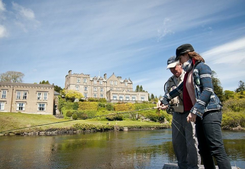 two women are standing near a body of water , with one of them holding a fishing rod at Ballynahinch Castle Hotel