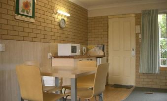 a small dining area with a table , chairs , and a microwave in a brick wall - covered room at Iluka Motel