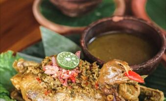 a delicious - looking roasted chicken dish with a green sauce and various toppings on a wooden table at Ubud Hotel & Cottages