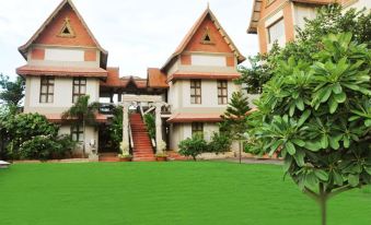 a large house surrounded by a grassy field , with stairs leading up to the front door at Aalankrita Resort and Convention