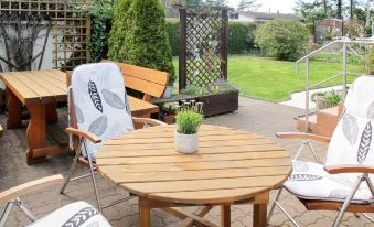 a wooden patio table and chairs set up for outdoor dining , surrounded by a lush green garden at Karli