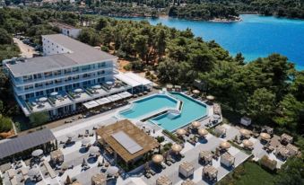 aerial view of a large resort with a swimming pool surrounded by lounge chairs and umbrellas , located near a lake at Valamar Meteor Hotel