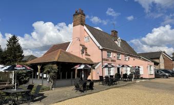 a pink building with a white roof , surrounded by tables and chairs outside , under a blue sky with clouds at Sorrel Horse Inn