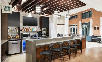 a modern bar with a long counter , several stools , and a television mounted on the wall at Hyatt Place Melbourne / Palm Bay / I-95