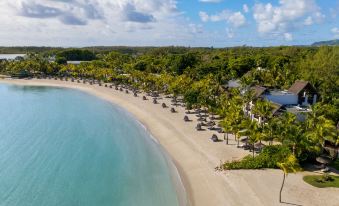 a tropical beach resort with umbrellas , chairs , and tables is nestled in a tropical setting at Shangri-La le Touessrok, Mauritius