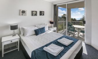 a bedroom with a large bed and white linens , next to a sliding glass door leading to a balcony at On the Beach Apartments