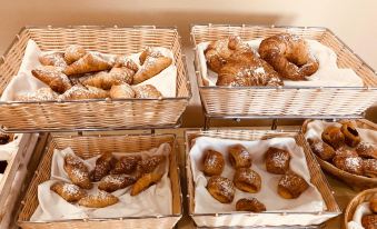 a dining table with a variety of pastries , including croissants , cakes , and donuts , neatly arranged in baskets at Hotel Valencia