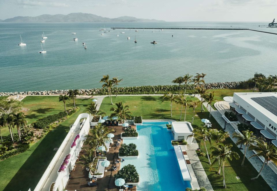 a rooftop pool surrounded by lush greenery , with a view of the ocean in the background at The Ville Resort - Casino