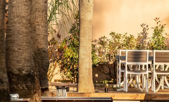 a group of wooden benches and chairs near a palm tree , with a restaurant in the background at Sea View Hotel & Apartments