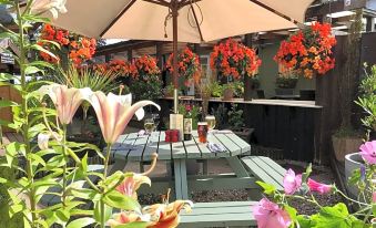 a patio area with a table and chairs , surrounded by potted plants and flowers , under an umbrella at Sibton White Horse Inn
