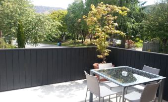 a patio with a dining table and chairs , surrounded by a black fence and trees at Arrowtown Motel