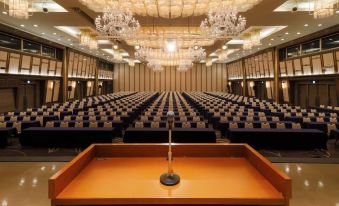 a large conference room with rows of chairs and a podium in the center , surrounded by chandeliers at Hotel Aomori