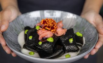 a woman is holding a bowl filled with various types of food , including sushi and other dishes at Mercure Milano Agrate Brianza