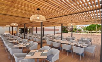 an outdoor dining area with wooden tables and chairs , surrounded by a brick wall and a patio at Protur Biomar Sensatori Resort