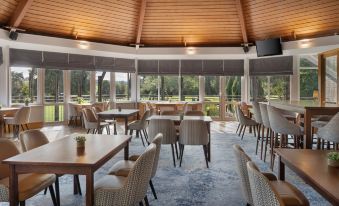 a spacious , well - lit restaurant with wooden tables and chairs , a curved ceiling , and large windows offering views of the outdoors at Delta Hotels Tudor Park Country Club
