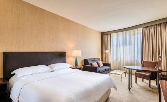 a large , well - made bed is the centerpiece of a hotel room with a couch and window at Sheraton Poznan Hotel