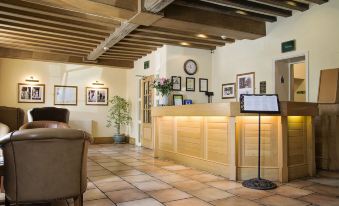 a well - lit reception area with wooden furniture , framed pictures on the wall , and a chair near the counter at Waveney House Hotel