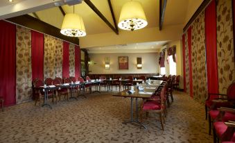 a large conference room with multiple tables and chairs , red curtains , and yellow pendant lights at Best Western Plus Pastures Hotel