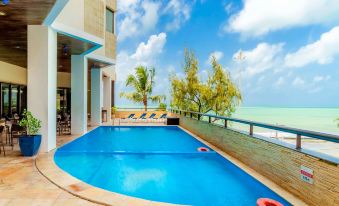 a large swimming pool is surrounded by a patio with lounge chairs and palm trees , overlooking the ocean at Grand Mercure Recife Boa Viagem