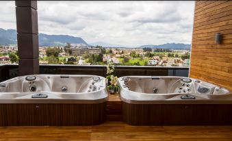 two large outdoor bathtubs placed on a wooden deck , with a beautiful view of the city and mountains in the background at Hotel Sabana Park