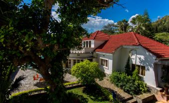 a beautiful white house with a red roof , surrounded by lush green trees and a stone pathway leading up to it at Belvedere Hotel