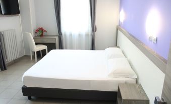 a white bed with a black headboard is in a room with a window and desk at Hotel Savoia