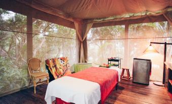 a luxurious tented room with a bed , couch , and chair under a large canopy , surrounded by trees at Ylang Ylang Beach Resort