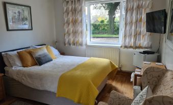 a cozy bedroom with a white bed , yellow blanket , and a window looking out onto a garden at Holm Oaks